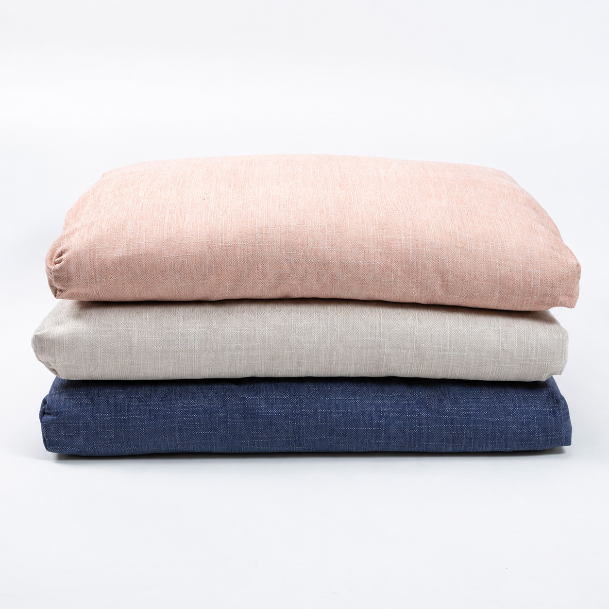 Three folded textured fabric cushions stacked vertically on a clean white background, in dusty pink, light beige, and navy blue.