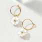 A pair of gold hoop earrings with dangling white flower charms, photographed on a clean white background with soft shadows.