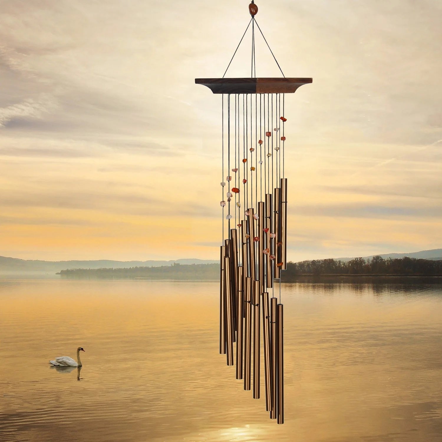 Wind chime hanging over a lake with a swan at sunset