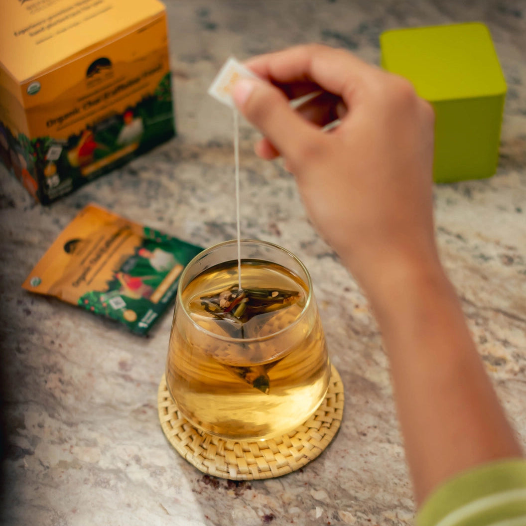 Person adding a tea bag to a glass of tea on a speckled countertop with tea packaging in the background.