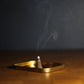 Incense cone burning on a gold tray with a dark background