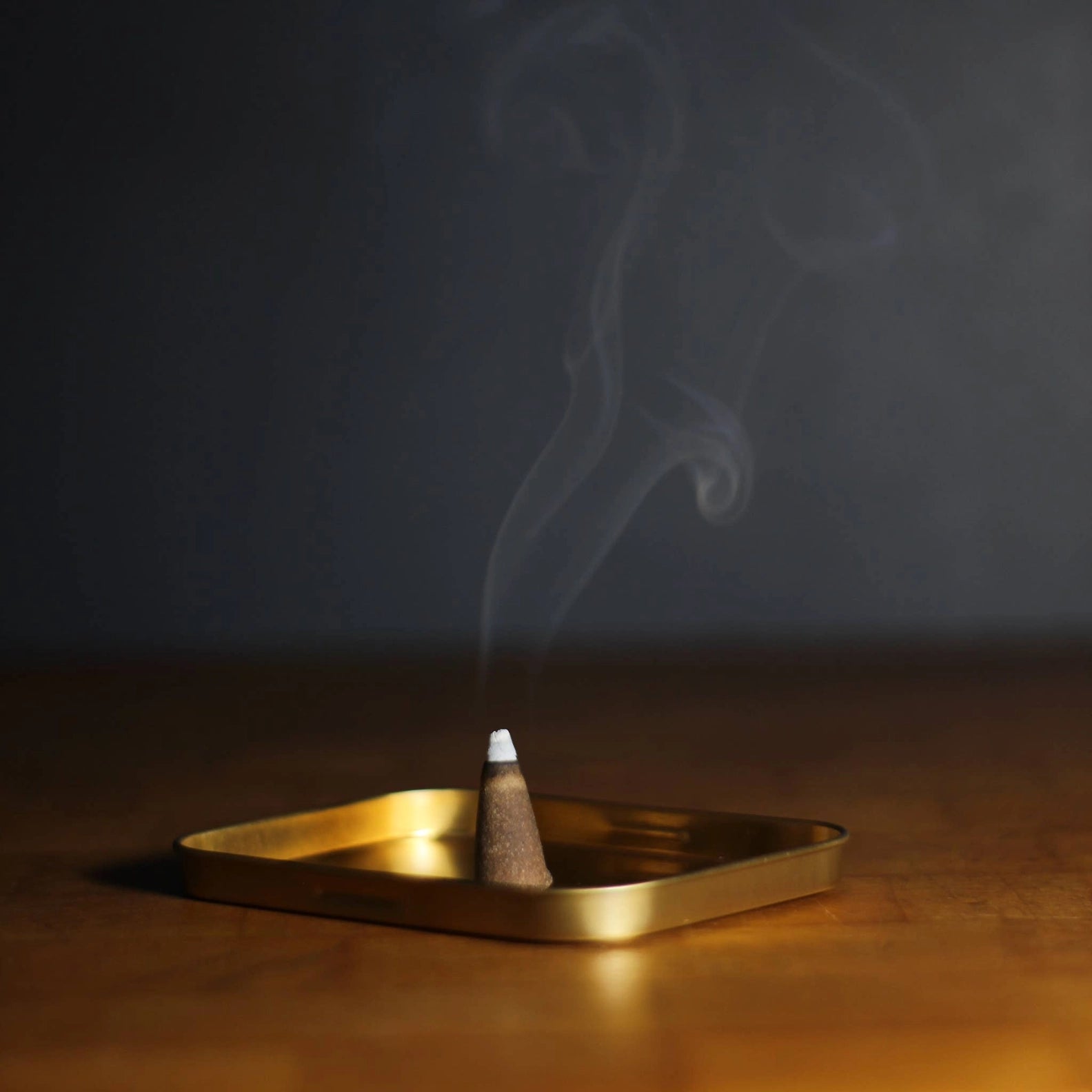 Incense cone burning on a gold tray with a dark background