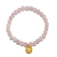 A pink faceted gemstone beaded bracelet with a gold-toned circular sunburst charm, displayed on a clean white background.