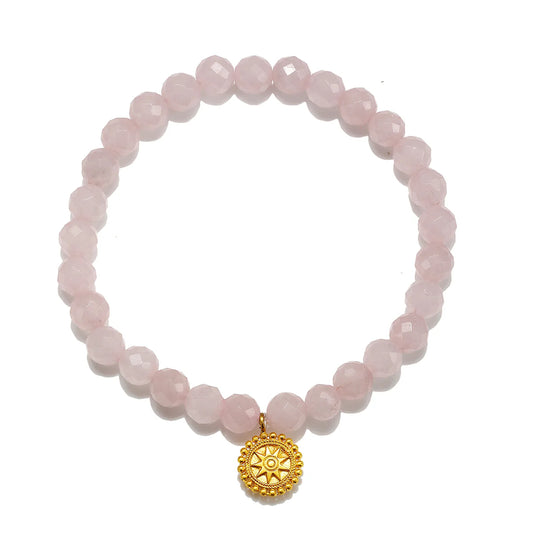 A pink faceted gemstone beaded bracelet with a gold-toned circular sunburst charm, displayed on a clean white background.
