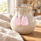 Rose quartz earrings hanging on a beige vase sitting on a wood table.