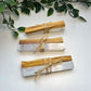 Three crystal sticks wrapped with palo santo on a white surface with green leaves.