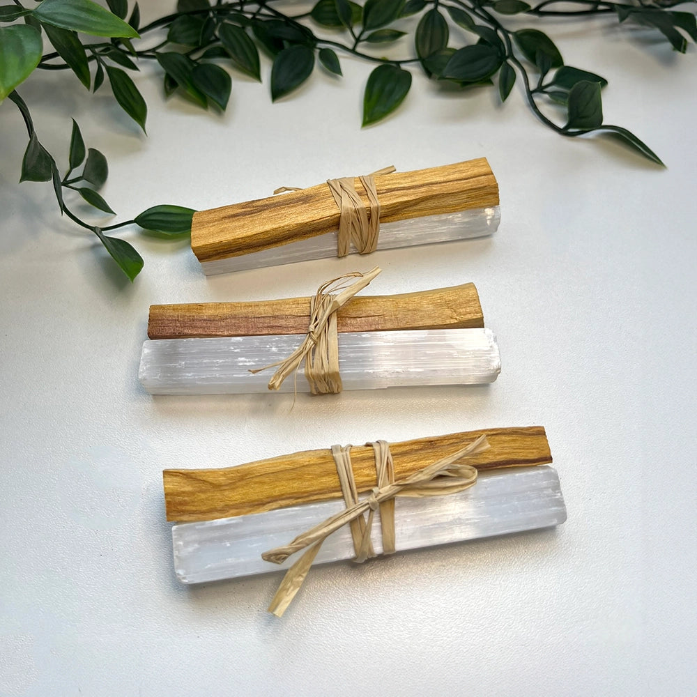Three crystal sticks wrapped with palo santo on a white surface with green leaves.