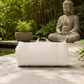 White cotton yoga mat on a stone surface with a Buddha statue and greenery in the background