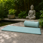 Teal yoga mat and rolled-up mat on a stone platform with a Buddha statue and garden in the background