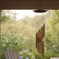 Decorative wind chime hanging from a wooden pergola with a blurred garden background
