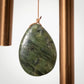 Green stone pendant hanging between two copper pipes on a white background