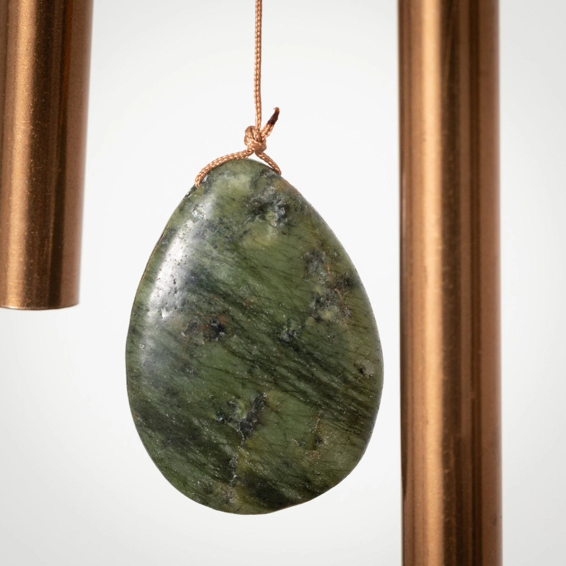 Green stone pendant hanging between two copper pipes on a white background