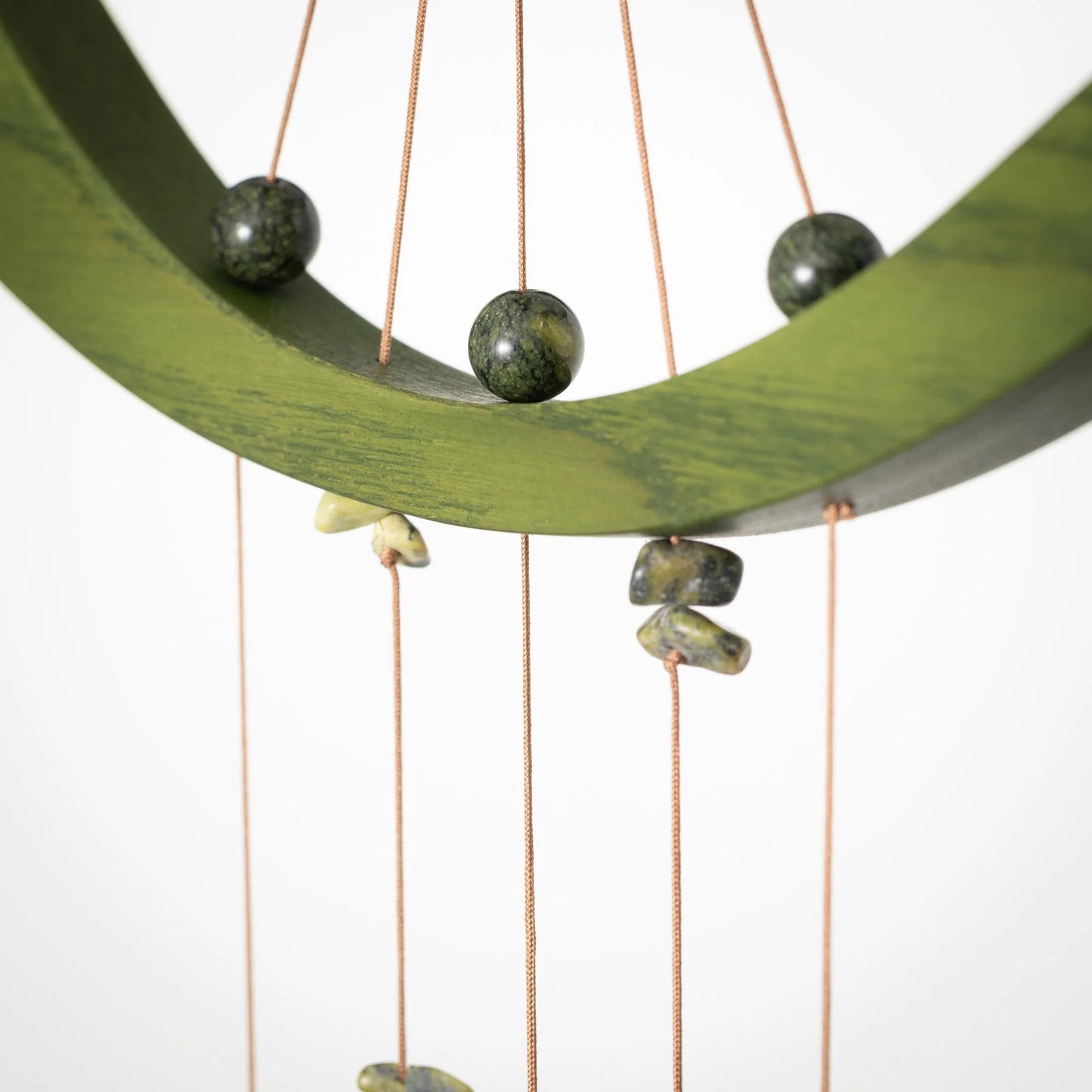 Decorative hanging with green stones and copper strings on a white background