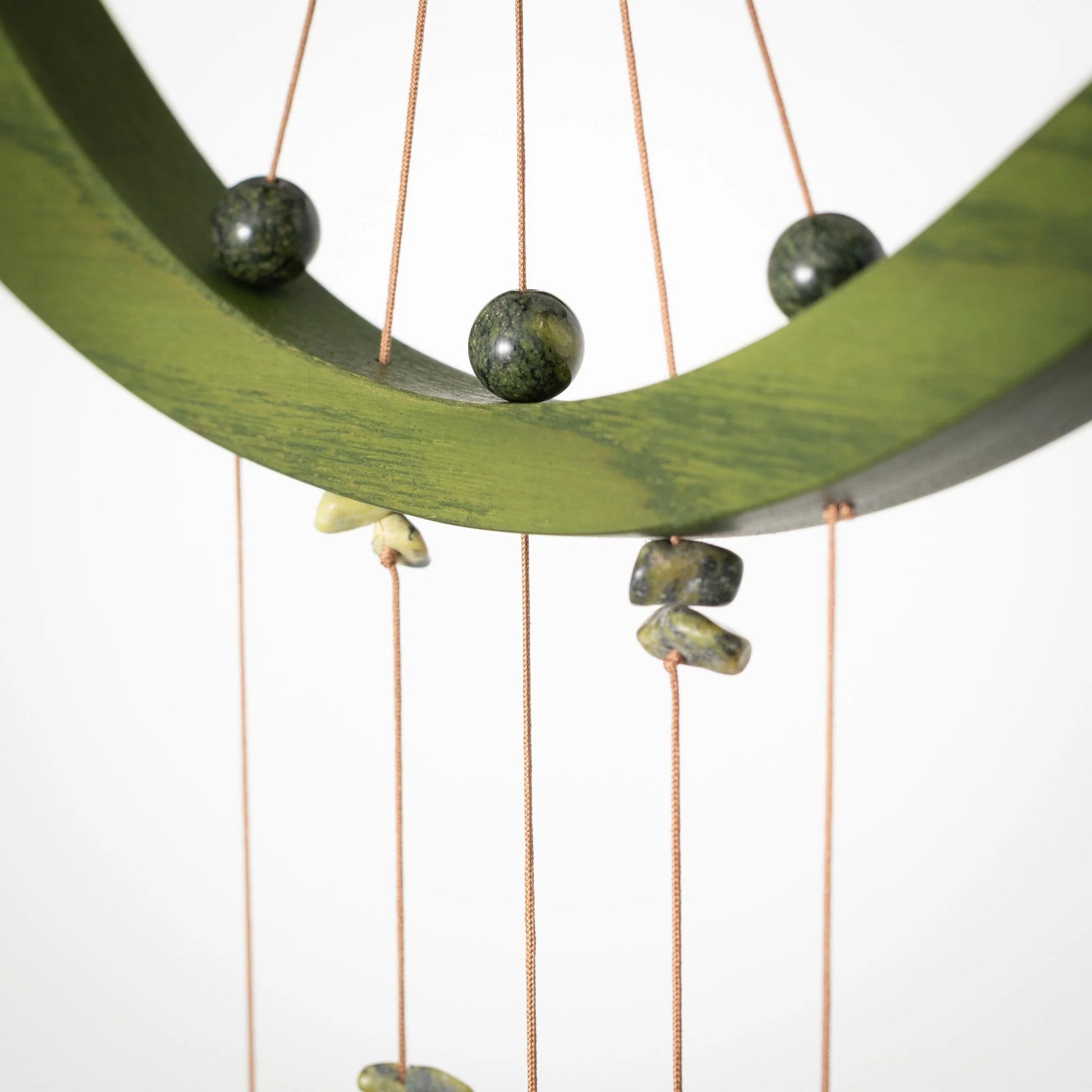 Decorative hanging with green stones and copper strings on a white background