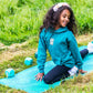 Child in a teal hoodie sitting on a yoga mat outdoors