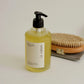 Bottle of yellow liquid soap with a pump and a brush on a light background