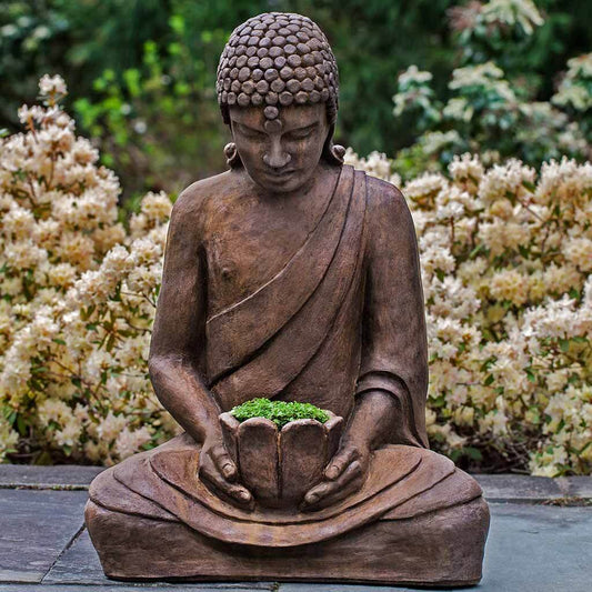Statue of a meditating Buddha holding a pot with plants against a garden background