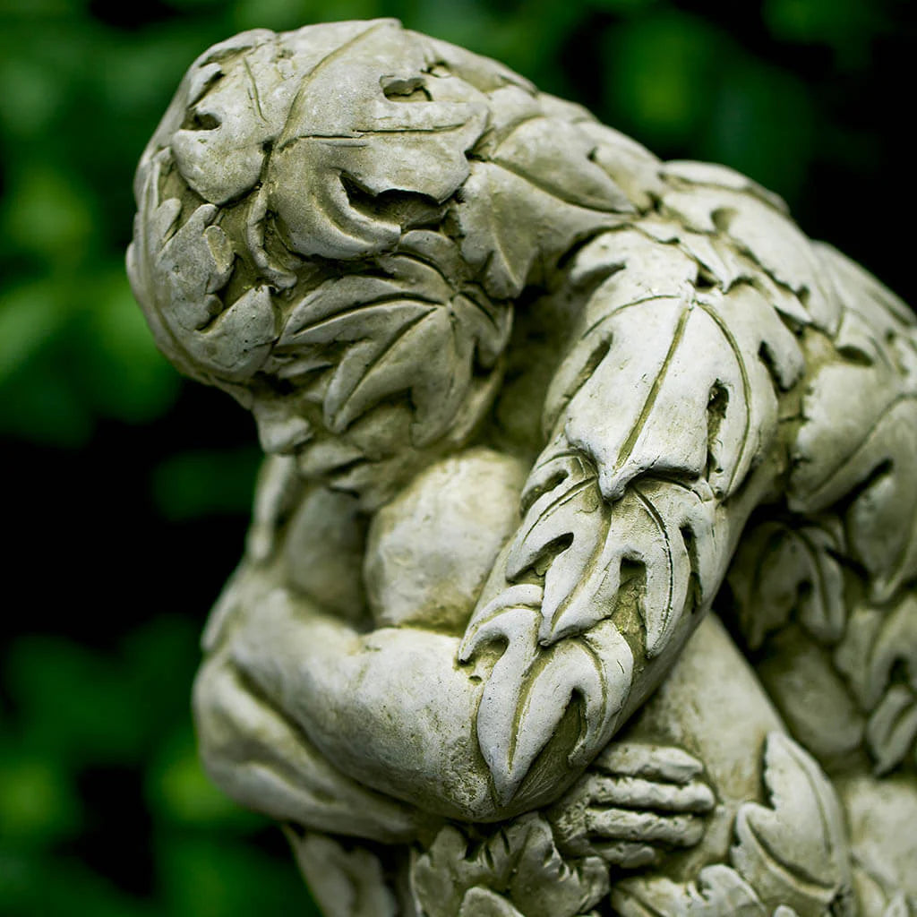 Stone sculpture of a figure with leaf-like patterns against a blurred green background