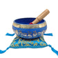 Medicine Buddha Singing Bowl rests atop our Lapis Brocade Singing Bowl Cushion, mallet inside, against a white backdrop.