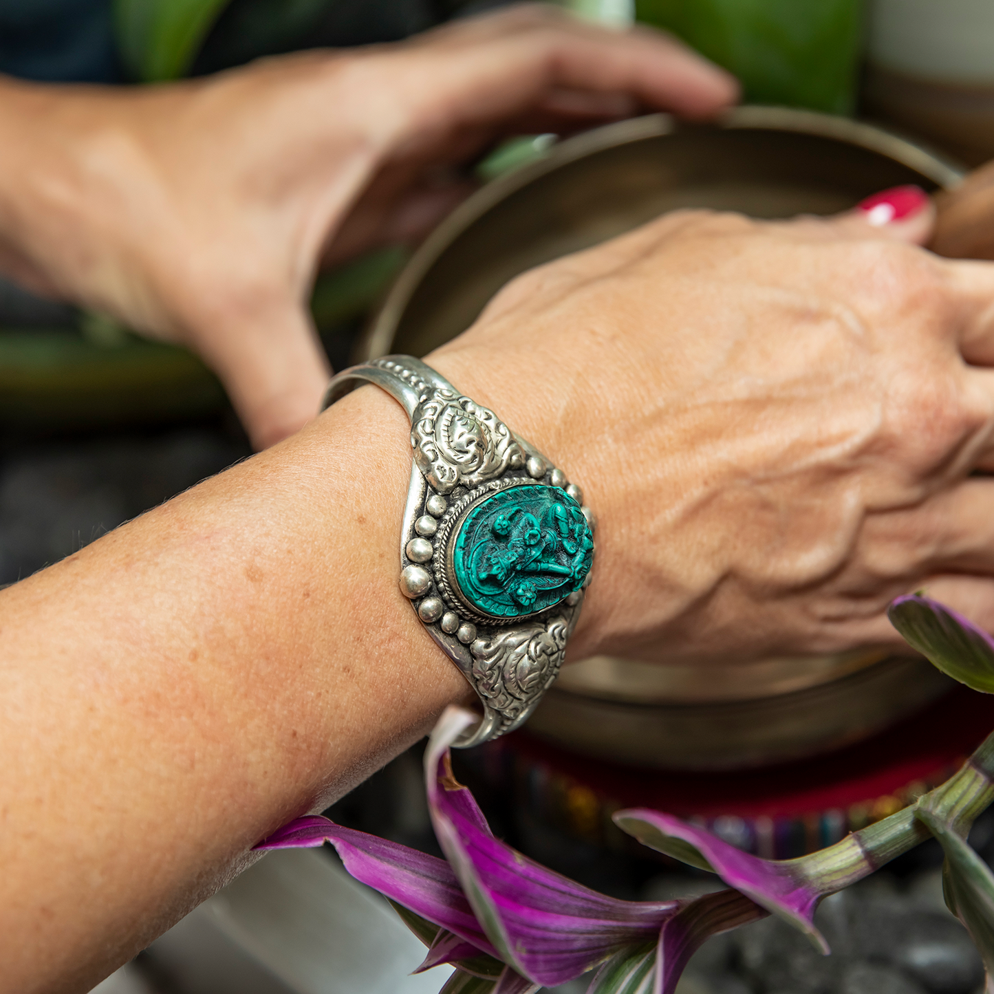Close-up of Green Tara Cuff Bracelet on a woman's wrist as she reaches for a singing bowl.