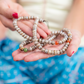 A woman's hands are outstretched- flat with palms up- presenting the Fresh Water Pearl Mala. Only the front beads are in focus.