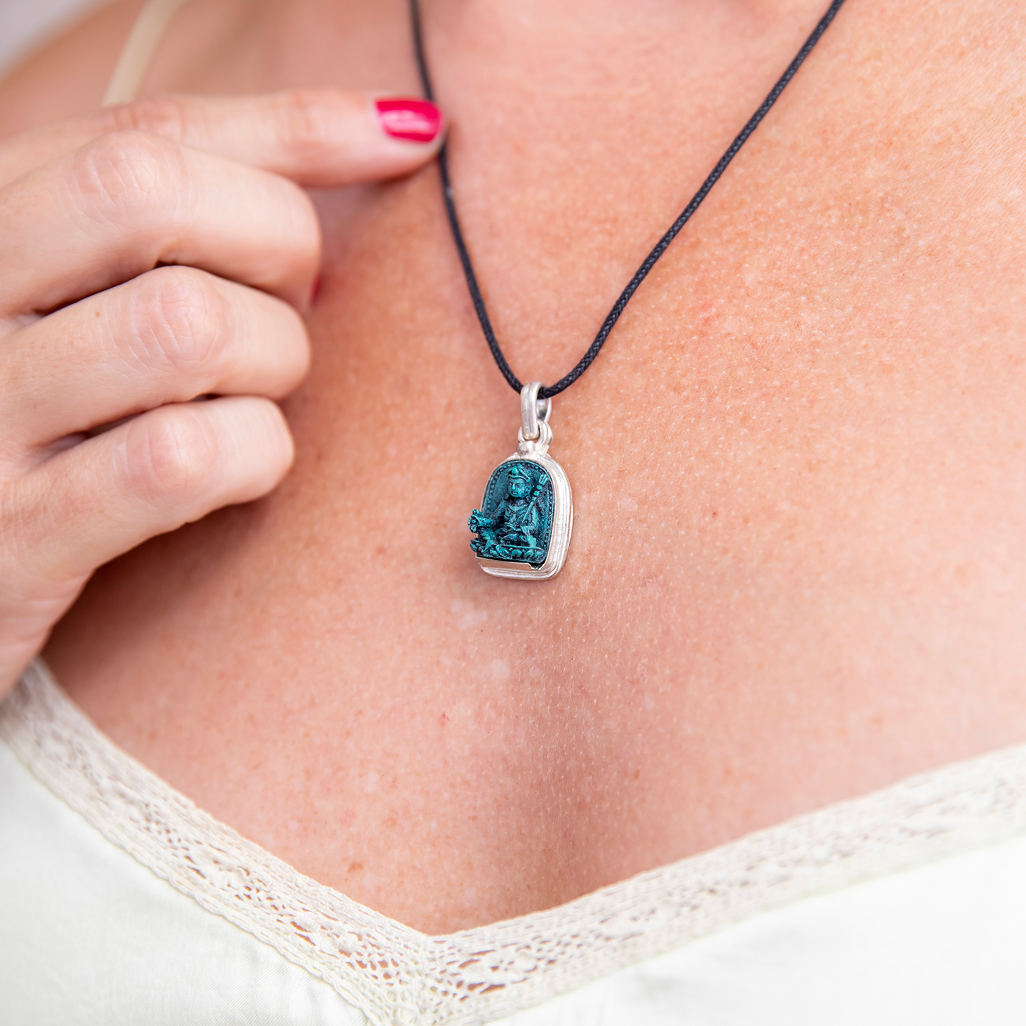 Close-up of Padmasambhava Pendant worn on a woman's chest. Her hand is in the photo, resting against her chest while her index finger lightly touches the cord of the necklace.