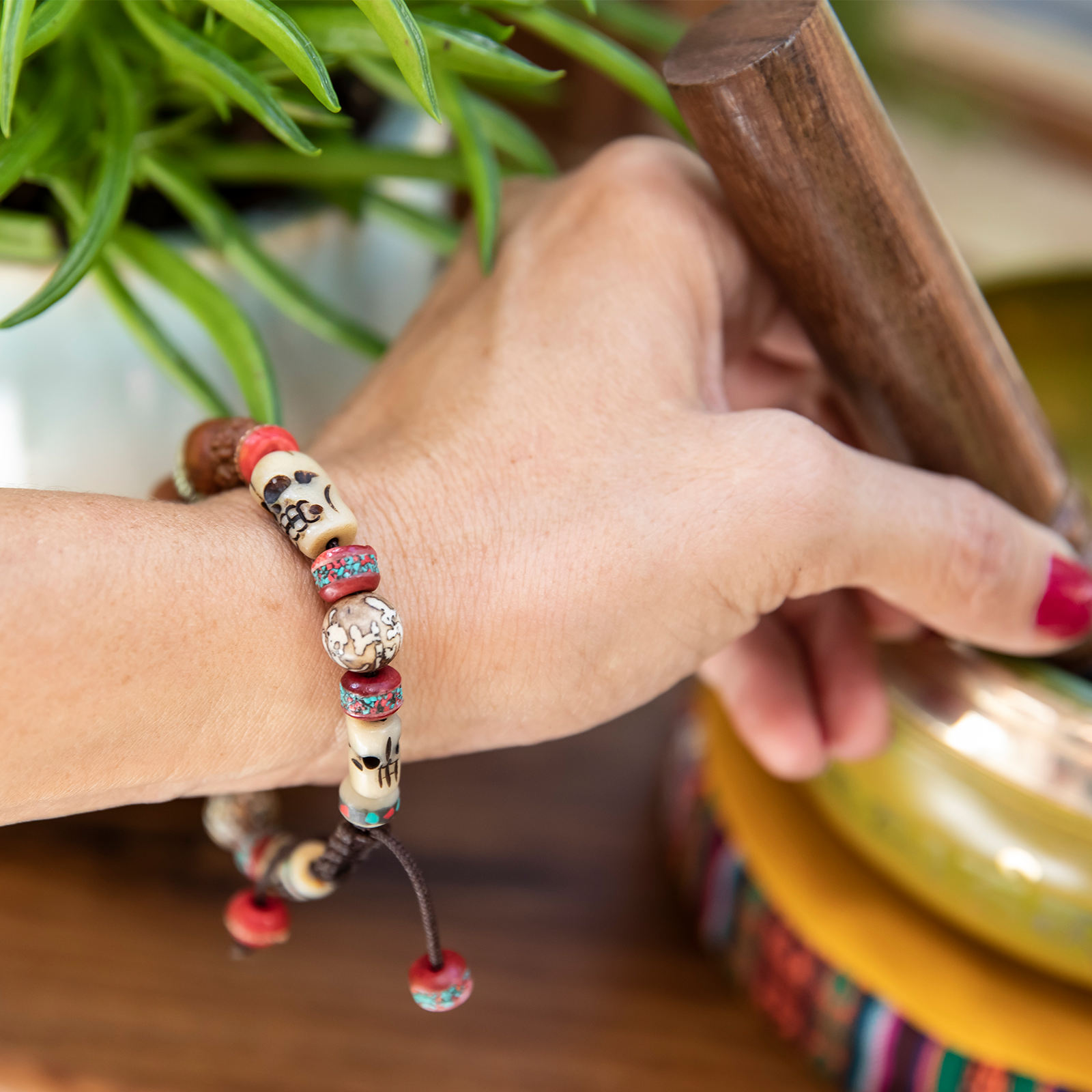 Close-up of woman's wrist wearing Shaman Bracelet as she reaches for a singing bowl mallet.