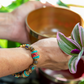 Close up of woman's wrist wearing the Prayer Wheel Bracelet. She is reaching for a bowl in a planter. Other bowls and foliage can be seen in the background.